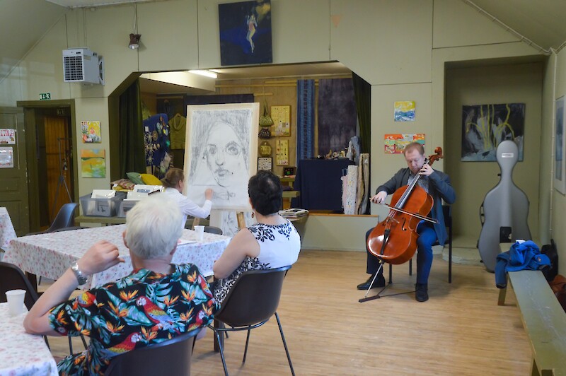 Taidetapahtumassa sellisti soittaa taiteilija piirtää yleisö seuraa istuen pöydissä